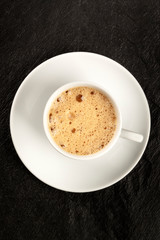 Poster - An overhead photo of a cup of coffee with foam on a black background with copy space