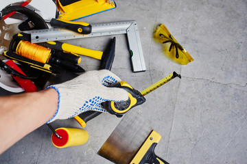 Wall Mural - The concept of repair. Male hand holding a tape measure against a background of construction tools. First person view.