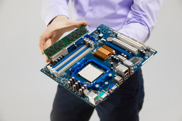 RAM and motherboard in men's hands close-up isolated on light background