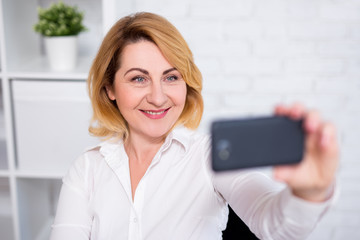 cheerful mature business woman taking selfie photo with smart phone