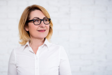 Wall Mural - portrait of thoughtful cheerful mature business woman in eyeglasses posing over white wall