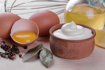 Mayonnaise in a wooden bowl and ingredients for making mayonnaise on a natural wooden background. white sauce.