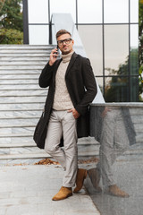 Canvas Print - Image of bearded man 30s wearing eyeglasses, walking through city street and using smartphone