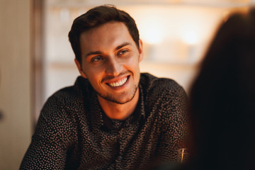 Wall Mural - Close up of a smiling man sitting at the table, looking at te woman