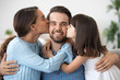 © fizkes - Cute kid daughter and loving wife embracing kissing young happy man on cheeks, caring beloved woman and little child girl congratulating dad husband with fathers day or birthday hugging smiling daddy
