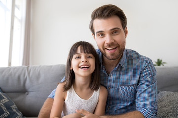 Wall Mural - Headshot of happy cute kid daughter and friendly smiling father looking on webcam talking at camera make online video call, child with dad record vlog together, daddy and little daughter portrait