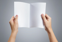Hands Holding A Sheet Of White Paper With Fold Line In The Middle On Gray Background