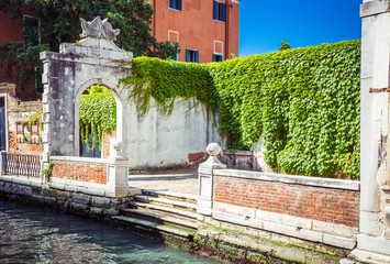 Wall Mural - Part of embankment with the old arch entwined with green plants on canal in Venice, Italy