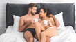 beautiful sexy couple lying with coffee cups in bed, smiling and looking at each other