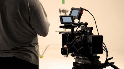 Behind video camera that recording online commercial or web film movie in the big studio production with professional equipment such as high resolution cam and monitors and LED light with crew team