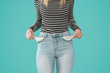 Young woman showing doesn't has nothing in her jeans pockets on blue background.