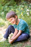 Fototapeta Dmuchawce - boy sitting on grass, enjoying hot summer day in nature, smiley happy face expression