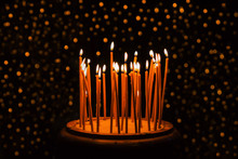Thin Yellow Candles Burning On The Black Background With Glitter Lights