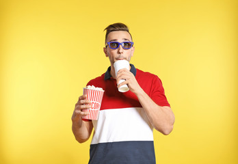 Canvas Print - Emotional man with 3D glasses, popcorn and beverage during cinema show on color background