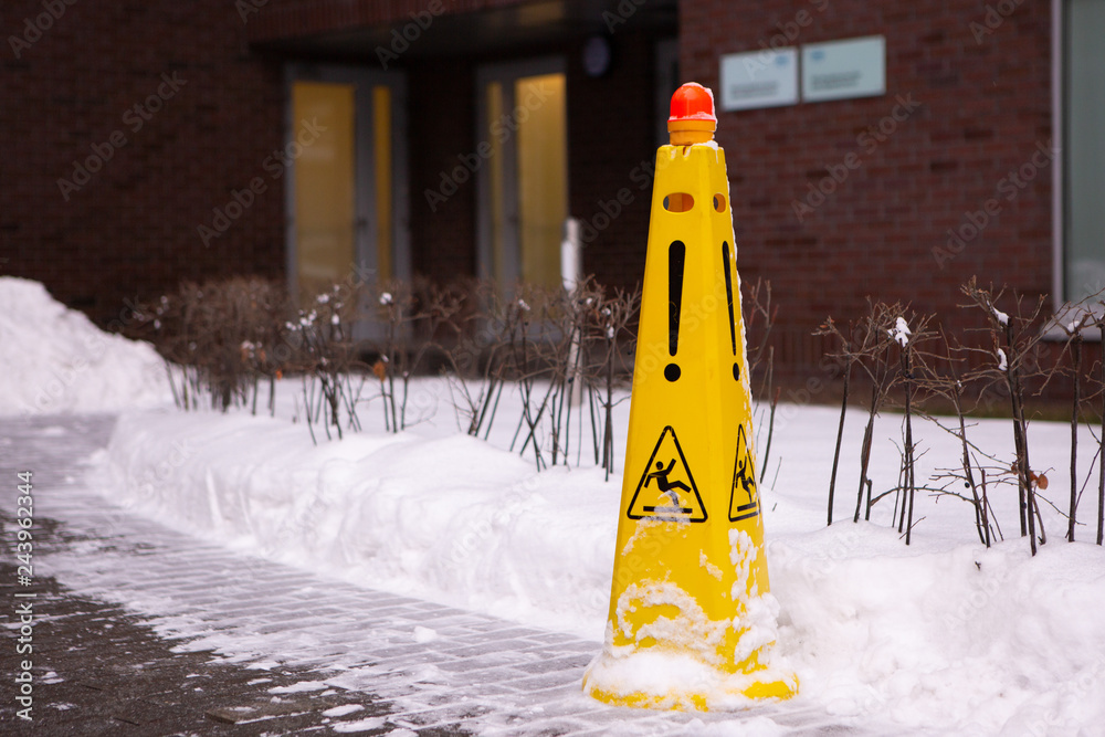 Caution Wet Floor. Slippery Yellow Surface Sign On Red Brick Building And Snow Heap. Slippery Slope. Icing Concept: Be Aware Of Slippery Road And Watch Your Step, Please. - obrazy, fototapety, plakaty 