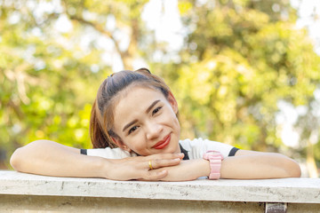 Asian woman with brown hair A small woman White skin, red lips Wearing a white shirt Sitting smile Comfortable on a white bench smile which trees in the park