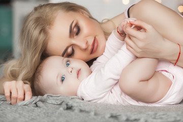 Wall Mural - Young pretty mother with her little baby at home. Mom and daughter indoors.  month child with her parent in the bedroom.