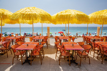 Yellow Umbrellas And Cafe Tables Line The Menton Promenade Facing The Beach