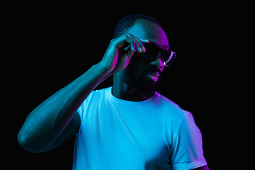 The retro wave or synth wave portrait of a young happy smiling african man in sunglasses at studio. High Fashion male model in colorful bright neon lights posing on black background. Art design