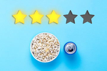 Bowl of popcorn and can with drink on a blue background. Added three stars rating. Reputation. Concept of watching movies, TV shows, sports. Audit and evaluation. Flat lay, top view.