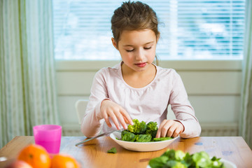 Cute girl eating spinach and broccoli at the table. Smiling and laughing happily. Healthy food concept. 