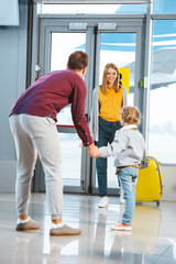 Wall Mural - cheerful mother looking at daughter and husband holding hands in airport