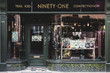 © Mint Images - Exterior view of interior design store with floral print cushions on vintage metal bench in shop window.