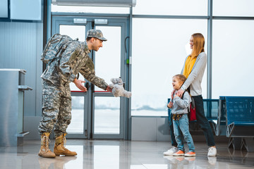 Wall Mural - dad in military uniform giving teddy bear to daughter standing near mother in airport