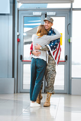 Wall Mural - cheerful veteran in military uniform hugging girlfriend in airport