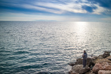 A Fisherman On A Blue Sea And Sky Stands On A Rock