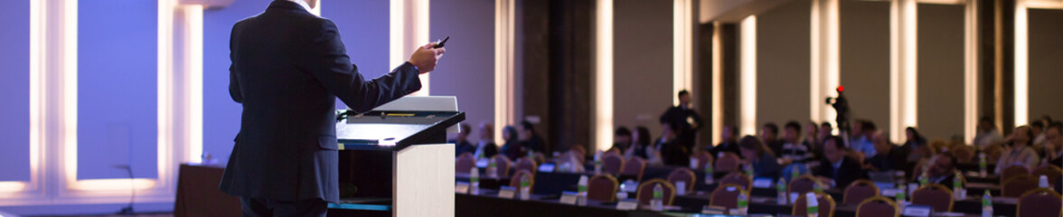 Fototapete - Speaker at Talk in Business Conference. Corporate Speaker on Stage at Seminar. Presenter Giving Business Presentation at Meeting. Corporate Exhibition for Investors Event.