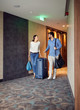 © luckybusiness - Man and woman arriving at hotel lobby with suitcase.