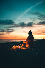 Wall Mural - Una ragazza sola è seduta sulla spiaggia al tramonto a osservare il mare e il cielo rosso per rilassamento.