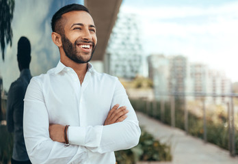portrait of a young confident smiling indian man with his arms crossed looking into the distance
