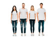 full length view of serious young men and women in white t-shirts and denim pants standing and looking at camera isolated on white