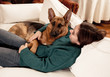 © SB Arts Media - Cute portrait of young woman and dog german shepherd hugging at cozy home in winter