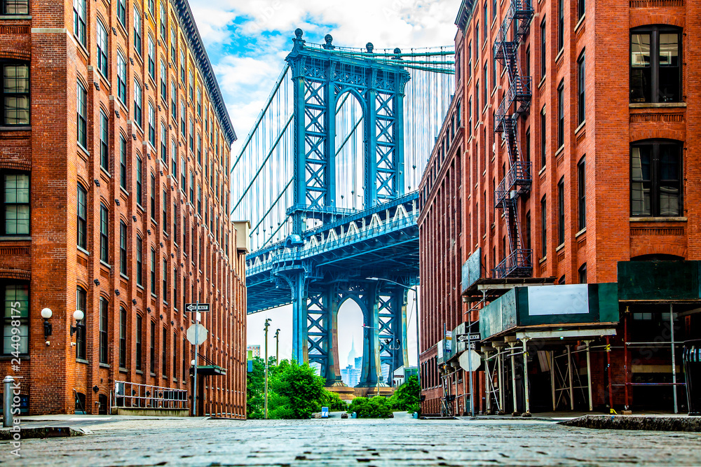 Manhattan Bridge between Manhattan and Brooklyn over East River seen from a narrow alley enclosed by two brick buildings on a sunny day in Washington street in Dumbo, Brooklyn, NYC - obrazy, fototapety, plakaty 