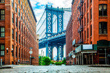 Manhattan Bridge between Manhattan and Brooklyn over East River seen from a narrow alley enclosed by two brick buildings on a sunny day in Washington street in Dumbo, Brooklyn, NYC