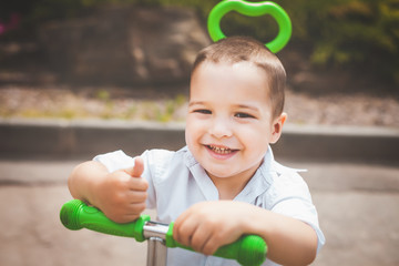 lovely small smiling infant boy riding a green trike in the park. concept of happy childhood