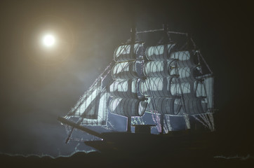 Wall Mural - Pirate ghost ship in a night smoky sea background.