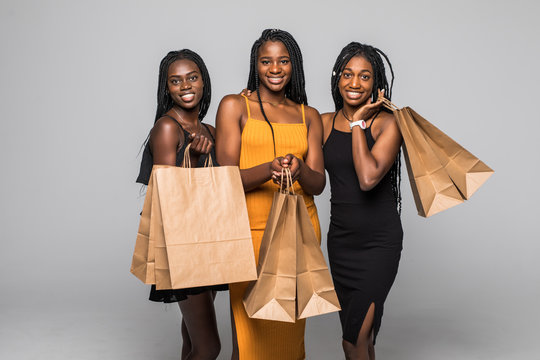 Portrait of three happy young african women wear in dresses holding shopping bags isolated over gray background