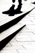 Blurry Silhouette Shadow Of A Man Walking On A City Sidewalk With Steps  In Black And White