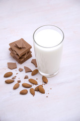 glass of milk next to chocolate pieces and almonds nuts on a wooden table 