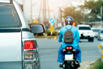 Silver pick up car open light break and motorcycle drivers with working uniform on the road stop by traffic junction on rush hour in the city. There is a car running from the opposite side, blurred.