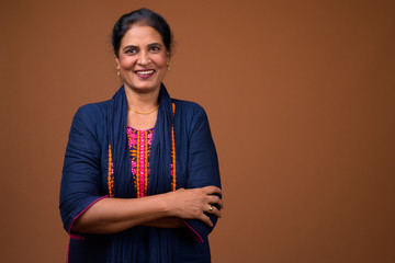 Happy mature Indian woman smiling against brown background