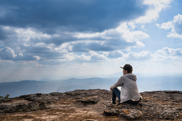 Wall Mural - A person sitting  on rocky mountain looking out at scenic natural view and beautiful blue sky