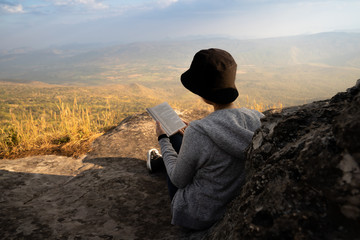 Wall Mural - Woman sitting reading and  looking out at beautiful natural view