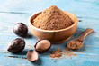 Whole inshell nut and nutmeg powder in a wooden bowl and spoon on old blue rustic background.