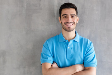 Wall Mural - Portrait of attractive young man in blue polo shirt, standing with crossed arms against gray textured wall