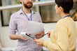© pressmaster - Young businesswoman with paper and pencil having talk to her colleague about analysis of financial rate